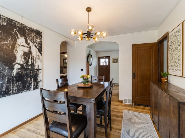 dining space with visible vents, arched walkways, and light wood-type flooring