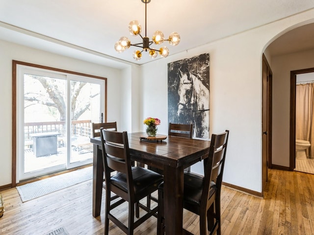 dining area with arched walkways, baseboards, a chandelier, and light wood finished floors