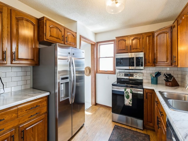 kitchen featuring a sink, light countertops, a textured ceiling, brown cabinetry, and stainless steel appliances