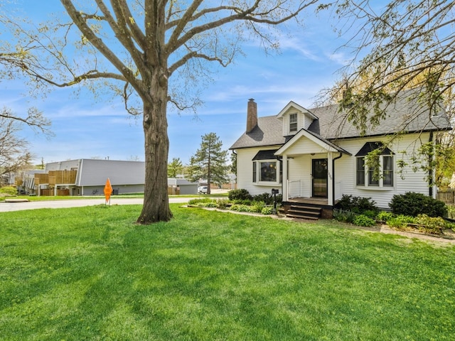 new england style home featuring roof with shingles, a chimney, and a front yard