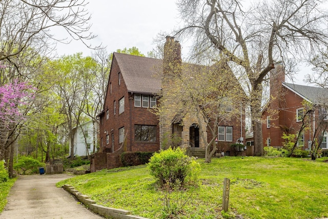 5502 Ingersoll Ave, Des Moines, IA 50312 - english style home featuring a chimney, a shingled roof, a front yard, and brick siding