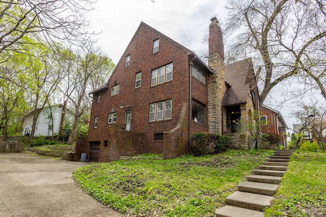 5502 Ingersoll Ave, Des Moines, IA 50312 - view of home's exterior with an attached garage, brick siding, stairway, a chimney, and driveway