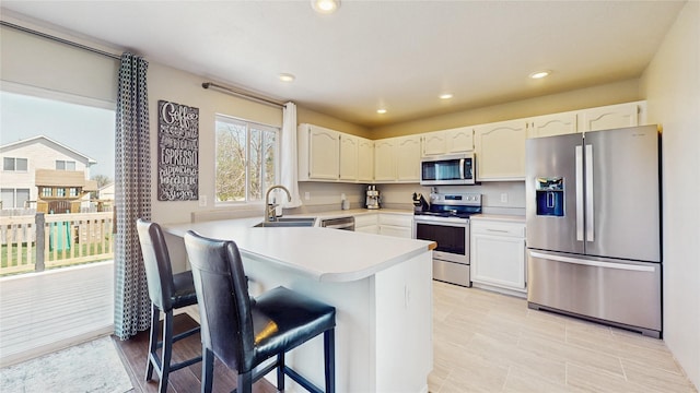 1009 SE 5th St, Grimes, IA 50111 - kitchen with stainless steel appliances, a peninsula, a sink, a kitchen bar, and light countertops