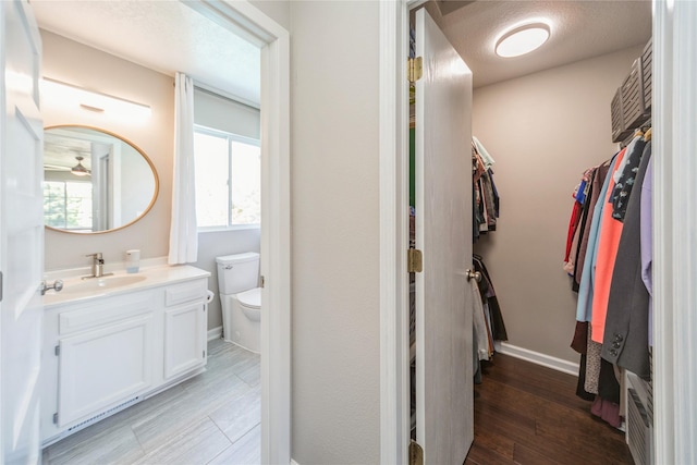1009 SE 5th St, Grimes, IA 50111 - bathroom with a walk in closet, vanity, wood finished floors, toilet, and baseboards