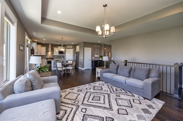 living room featuring visible vents, dark wood finished floors, a notable chandelier, a tray ceiling, and recessed lighting