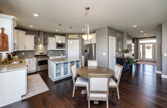 kitchen with wall chimney range hood, a center island, tasteful backsplash, a sink, and stainless steel appliances