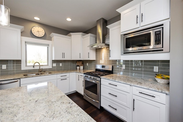 kitchen featuring appliances with stainless steel finishes, a sink, dark wood finished floors, wall chimney exhaust hood, and white cabinetry