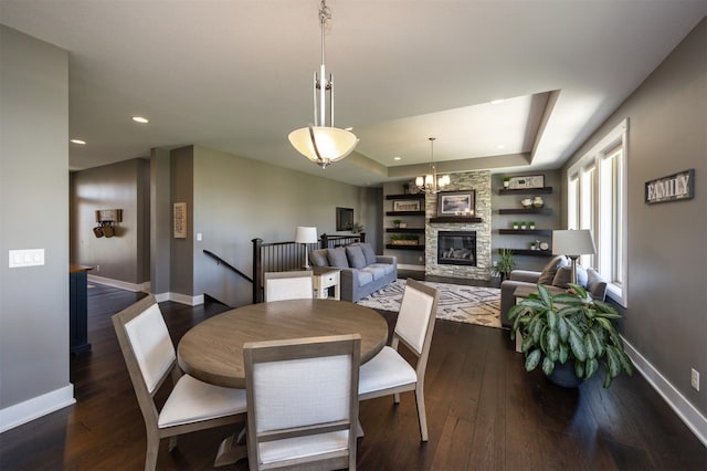 dining room with dark wood-style flooring, baseboards, recessed lighting, and a stone fireplace