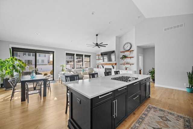 970 Roman Rd, Waukee, IA 50263 - kitchen with ceiling fan, stainless steel gas cooktop, dark cabinets, light wood-style flooring, and a center island