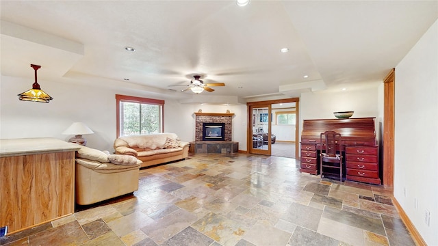 living room featuring ceiling fan, baseboards, stone tile flooring, a glass covered fireplace, and recessed lighting