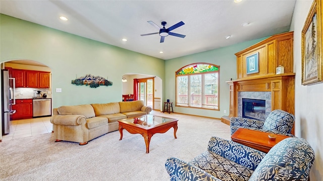 living room with arched walkways, ceiling fan, light carpet, and a tile fireplace