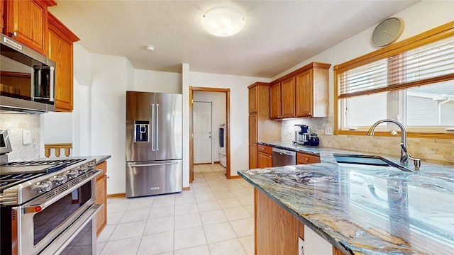 kitchen with dark stone counters, stainless steel appliances, a sink, and backsplash