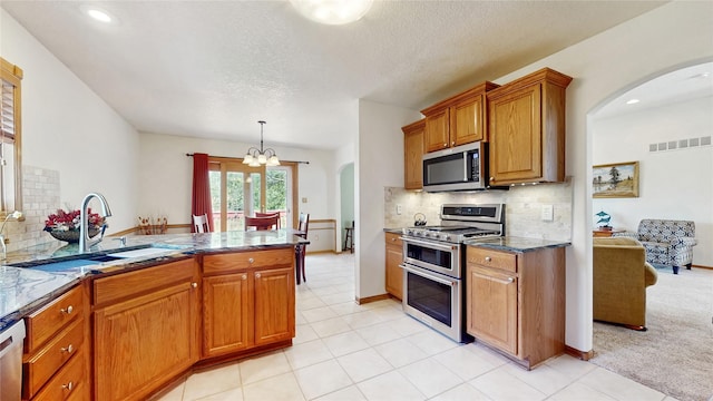 kitchen with brown cabinets, an inviting chandelier, a sink, stainless steel appliances, and visible vents