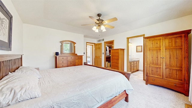 bedroom featuring visible vents, ensuite bathroom, a walk in closet, light colored carpet, and a ceiling fan