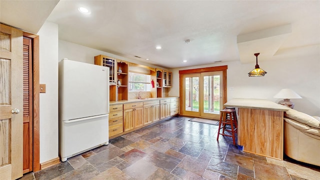 kitchen with stone tile flooring, freestanding refrigerator, recessed lighting, and light countertops