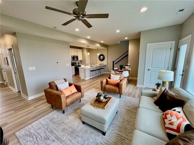 living room featuring stairway, baseboards, light wood-style floors, and a ceiling fan