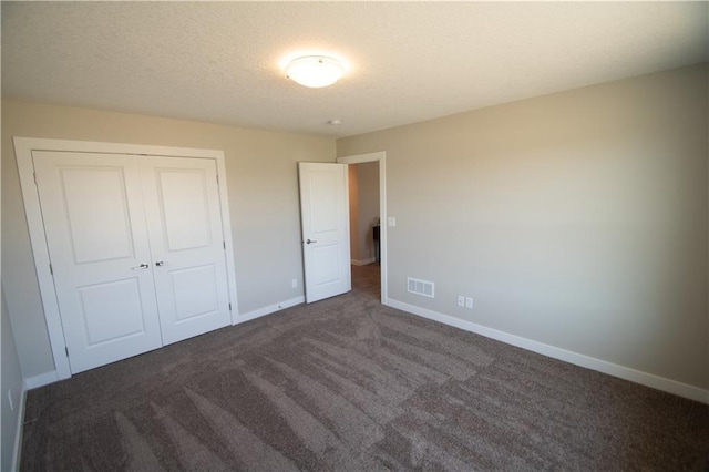 unfurnished bedroom with a textured ceiling, dark colored carpet, baseboards, visible vents, and a closet