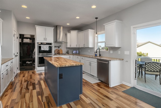 7517 NW 97th Ct, Johnston, IA 50131 - kitchen featuring appliances with stainless steel finishes, butcher block countertops, wall chimney range hood, light wood finished floors, and a center island