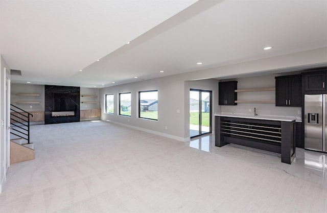unfurnished living room featuring indoor wet bar, baseboards, stairway, recessed lighting, and a premium fireplace
