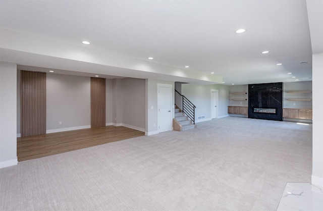 finished basement featuring light colored carpet, a premium fireplace, stairs, recessed lighting, and baseboards
