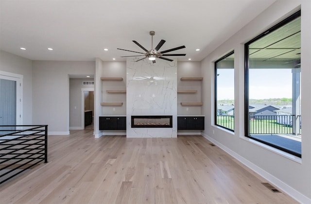 unfurnished living room featuring a premium fireplace, ceiling fan, visible vents, and light wood-style floors