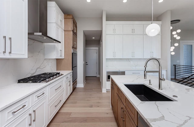 kitchen with a sink, light wood finished floors, wall chimney exhaust hood, stainless steel gas stovetop, and tasteful backsplash