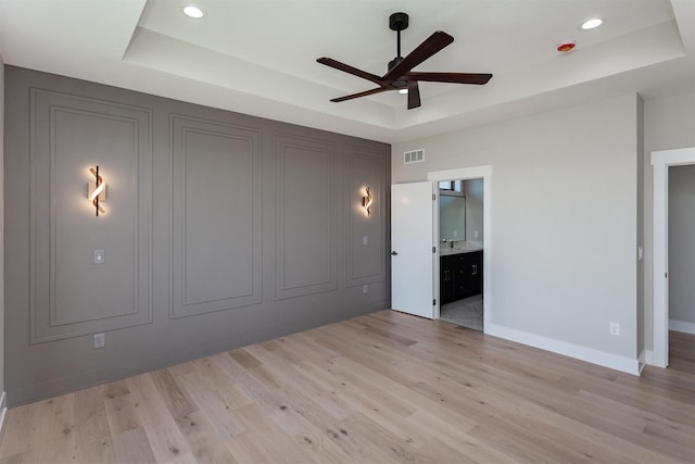 unfurnished bedroom featuring a raised ceiling, light wood finished floors, and visible vents