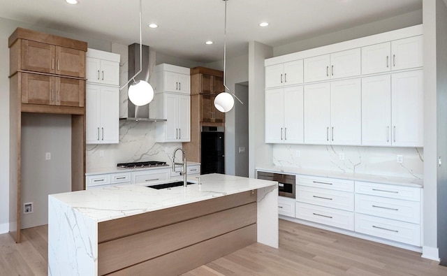 kitchen with a sink, wall chimney range hood, recessed lighting, and light wood-style flooring