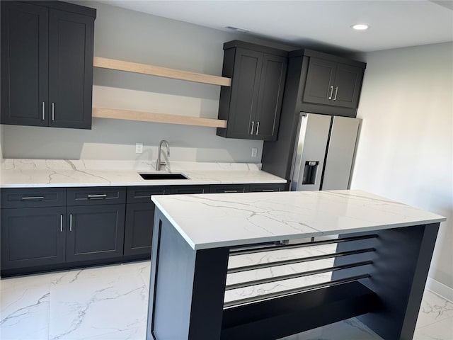 kitchen featuring open shelves, light stone countertops, a sink, marble finish floor, and stainless steel fridge