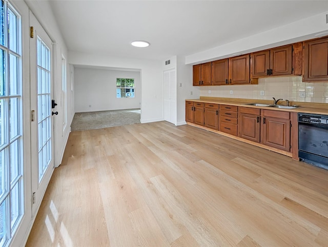 kitchen with brown cabinetry, light wood-type flooring, light countertops, a sink, and dishwasher