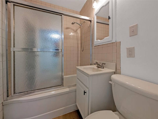 full bath with tile walls, wood finished floors, vanity, combined bath / shower with glass door, and toilet