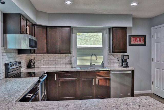 kitchen with dark brown cabinets, appliances with stainless steel finishes, a sink, recessed lighting, and wood finished floors