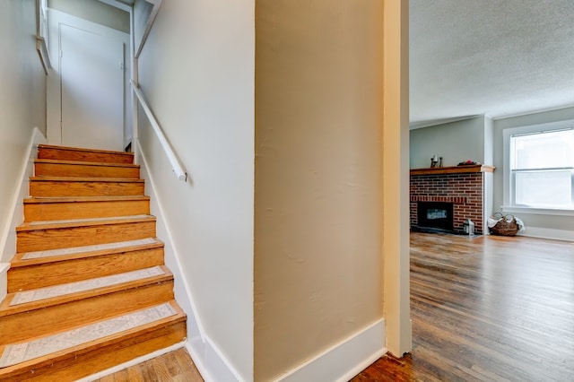 stairway with baseboards, a textured ceiling, wood finished floors, and a fireplace