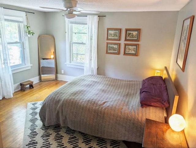 bedroom with ceiling fan, baseboards, multiple windows, and wood finished floors