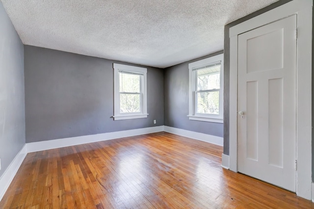 empty room featuring wood-type flooring, a textured ceiling, and baseboards