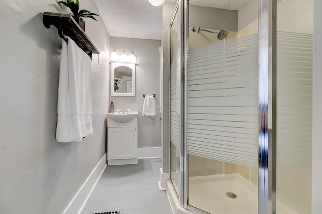 bathroom with baseboards, a textured ceiling, a stall shower, and vanity