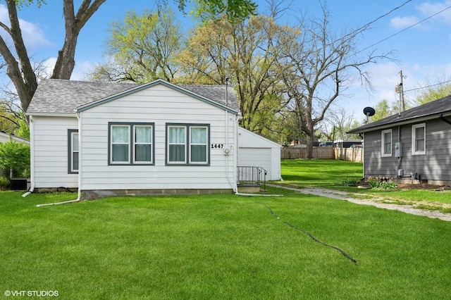 rear view of house with fence, a shingled roof, a lawn, and a garage