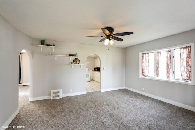 empty room with arched walkways, ceiling fan, light carpet, and baseboards