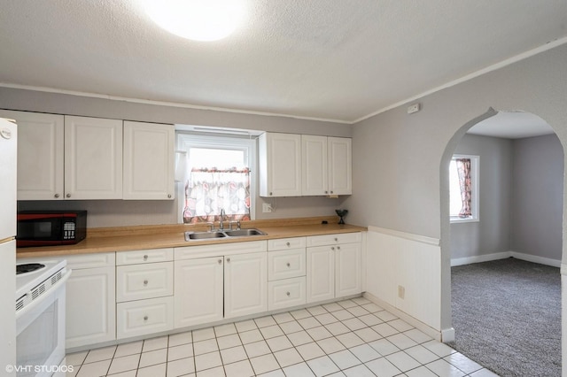kitchen with black microwave, arched walkways, a sink, white cabinets, and white range with electric stovetop