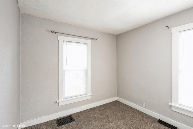spare room featuring baseboards, visible vents, and dark colored carpet
