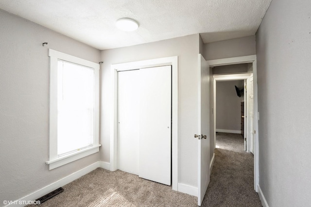 unfurnished bedroom featuring a textured ceiling, visible vents, carpet floors, baseboards, and a closet