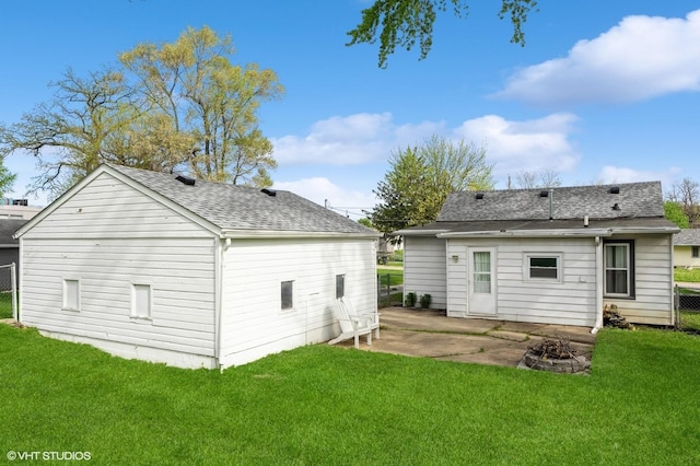 back of property with a lawn, a shingled roof, fence, a patio, and a fire pit
