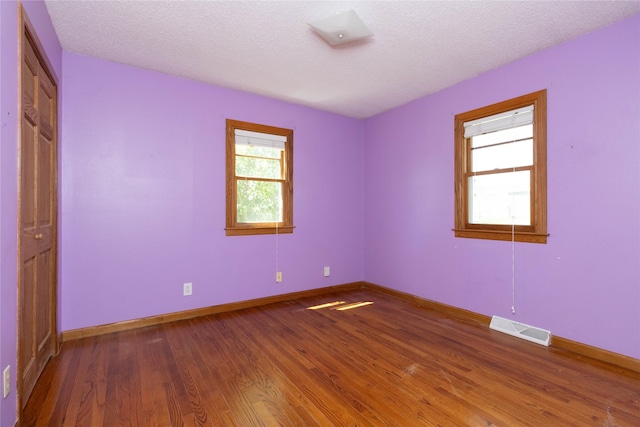 empty room with a textured ceiling, baseboards, visible vents, and wood finished floors