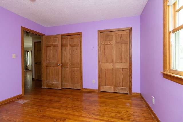 unfurnished bedroom with baseboards, a textured ceiling, light wood finished floors, and two closets