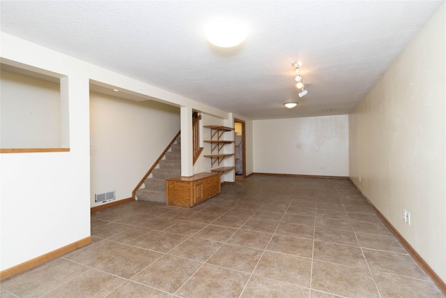 finished basement with a textured ceiling, baseboards, light tile patterned floors, visible vents, and stairway