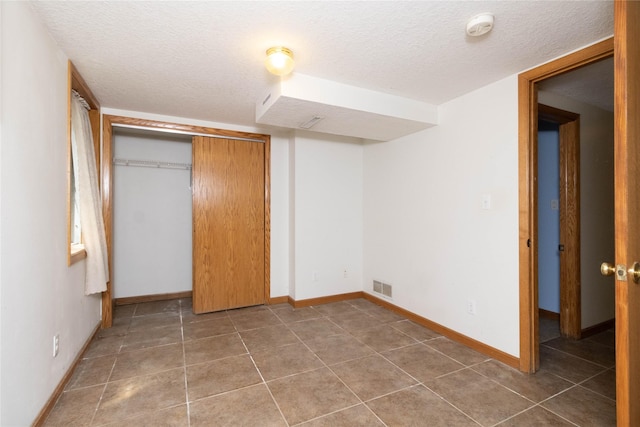 unfurnished bedroom featuring visible vents, tile patterned flooring, a closet, baseboards, and a textured ceiling