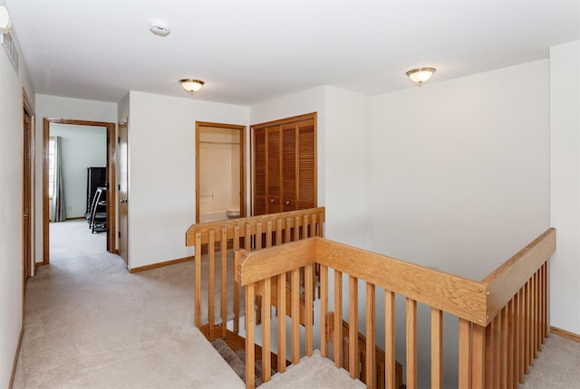 corridor featuring baseboards, light carpet, and an upstairs landing