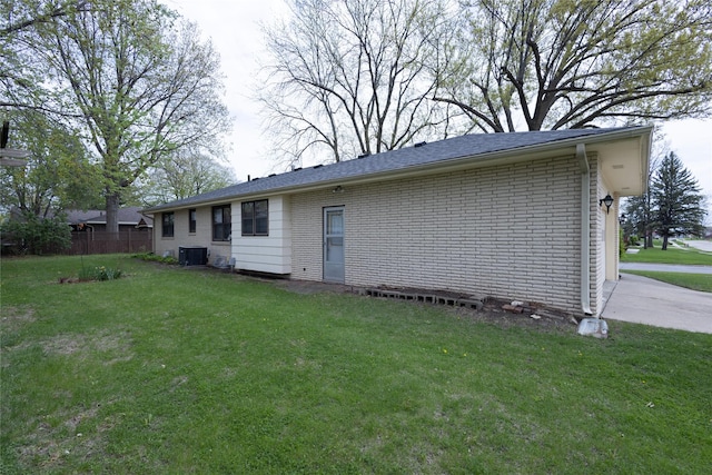 rear view of house featuring brick siding, a lawn, central air condition unit, and fence
