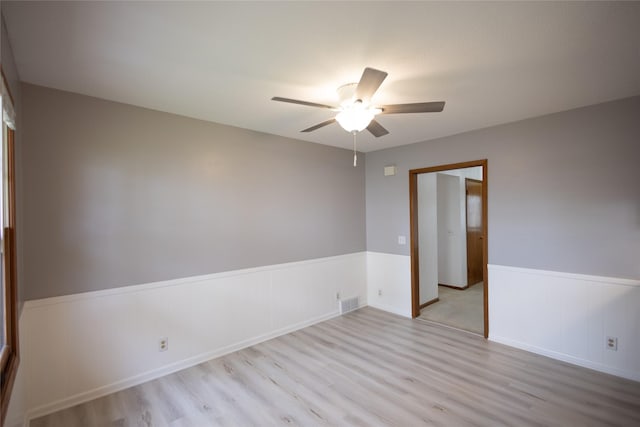 spare room with ceiling fan, visible vents, wainscoting, and light wood-style floors