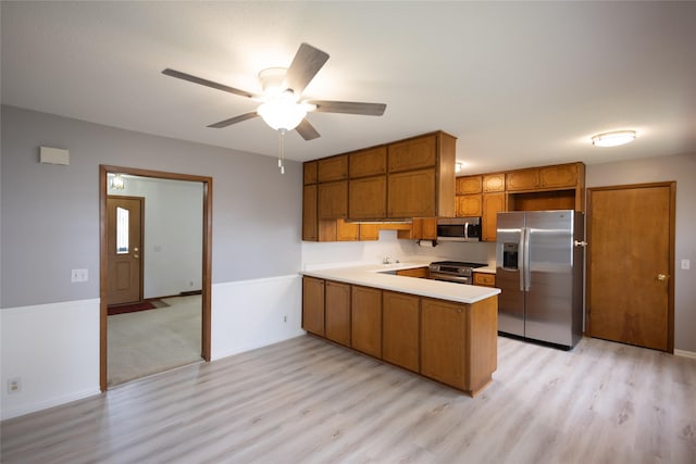 kitchen featuring appliances with stainless steel finishes, light wood finished floors, a peninsula, and brown cabinetry